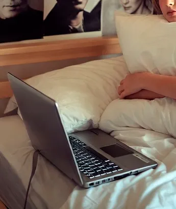 Человек лежит в постели с ноутбуком, опираясь на подушку